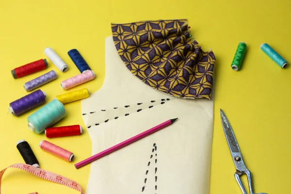 Sewing accessories and fabric on a yelow background. Sewing threads, pins, pattern and sewing centimeter. For sewing at home.Top view, flatlay