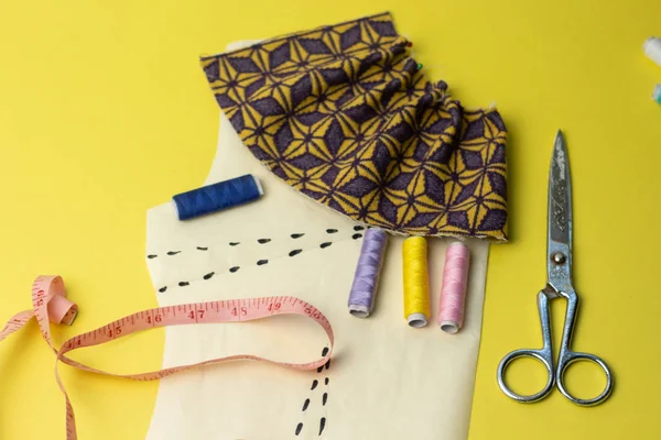 Bir yelow arka plan üzerinde dikiş aksesuarları ve kumaş. Dikiş iplikleri, pimleri, desen ve dikiş santimetre. Evde dikiş diktiğiiçin. Üst tenli, düzlük