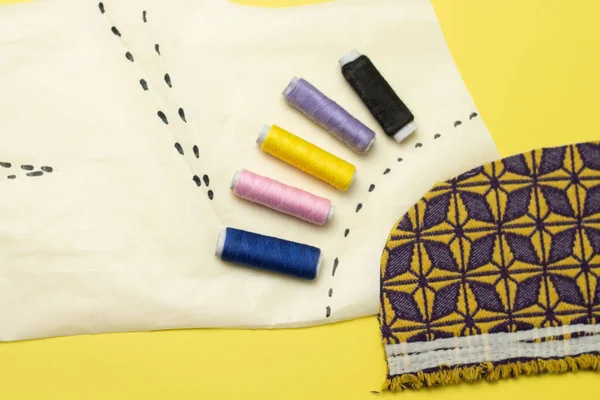 Sewing accessories and fabric on a yelow background. Sewing threads, pins, pattern and sewing centimeter. For sewing at home.Top view, flatlay