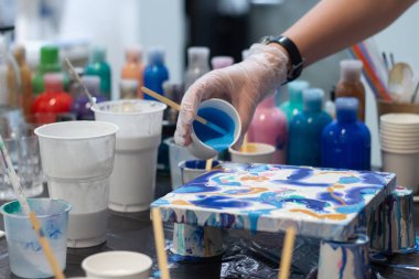 Sanatçının elleri yeni projesi için akrilik boyayı karıştırıyor, farklı renkler. Gerçek sanat ve ilham için sanatçı araçları. Arka planda sanat stüdyosu.