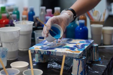 Sanatçının elleri yeni projesi için akrilik boyayı karıştırıyor, farklı renkler. Gerçek sanat ve ilham için sanatçı araçları. Arka planda sanat stüdyosu.