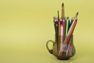 Sarı üzerine izole edilmiş şeffaf bir cam kupa içinde çok renkli kalemler. Çocuk yaratıcılığı.