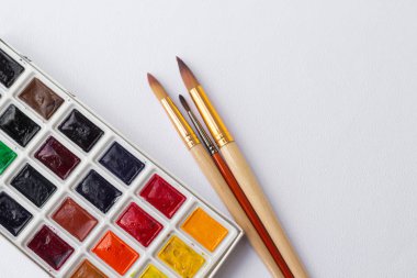 Renkli kuru suluboya tablet seti ve beyaz plastik palet ve beyaz doku arka plan, sanat ve eğitim nesnesi üzerinde boya fırçaları ve kalemler. Ön görünüm