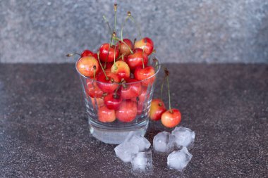 Viski bardağında sarı kirazlar, buz küpleri ve bir şişe viski. Viskinin dibinde ferahlatıcı soğuk bir kokteyl..