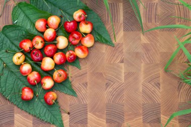 Yeşil çimenli bir arka planda, ahşap bir kesme tahtasının üzerinde sarı, tatlı bir kiraz. Yakın plan. Boşluğu kopyala.