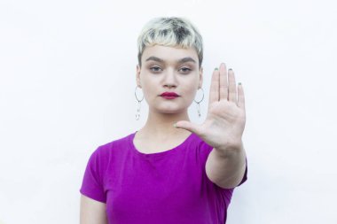 Sarışın bir kadın parmaklarıyla işaret veriyor. Sessiz ve ciddi bir ifade takınıyor. Durma hareketi gösteriyor.