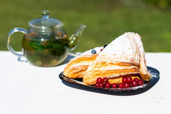 Delicious breakfast with fresh croissants and ripe berries and mint tea on the background of green grass. Summer breakfast time.