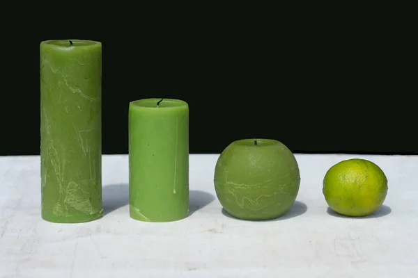 three lime-colored candles and one lime on white wooden table