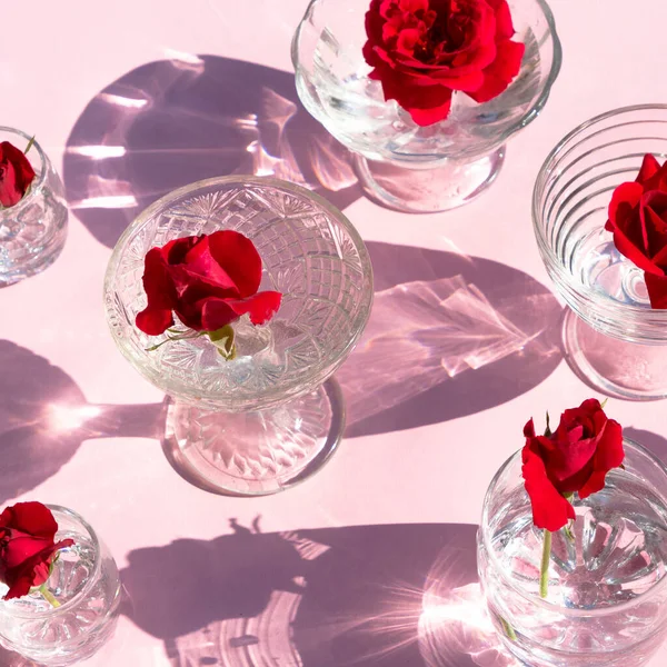 Очки Прозрачной Водой Красные Розы Стоят Розовом Фоне Вид Сверху — стоковое фото