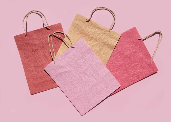 Colourful textured paper shopping bags on pink background. Minimal fashion shopping online concept. Copy space, top view, flat lay. Mock up.
