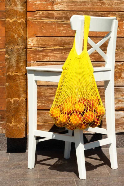 A mesh bag or string bag with ripe peaches on the back of a white chair. Zero waste.