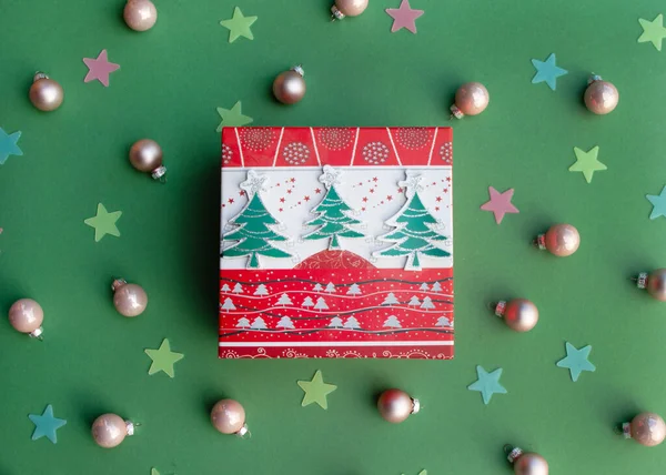 ピンクのボールとカラフルな星と緑の背景にクリスマスツリーと手作りのギフトボックス。ギフトボックスプレゼントを飾るとメリークリスマスのコンセプト. — ストック写真