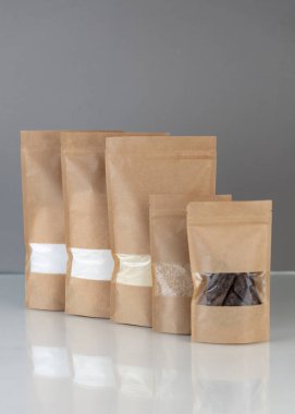 Brown kraft paper doypack bags with groceries front view on gray background. Packaging for foods and goods template mock-up. Packs with windows for weight products. clipart