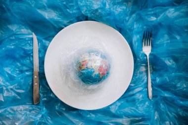 Seyyare yerküre plastik bir plaka üzerinde bir çatal ve bıçak bir insan tarafından yemiş kaplı. Plastik kirliliği ve atık kavramı. İnsan etkisi - çöp plastik. Küresel ısınma sorunu. 