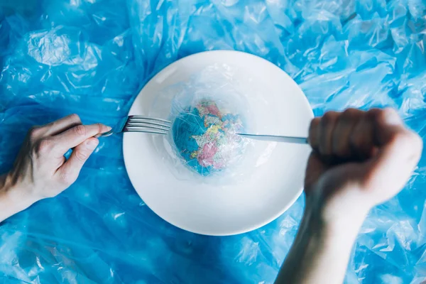 Planet Earth covered in plastic on a plate with a fork and knife eaten up by a human. Plastic pollution and waste concept. Human Impact - Refuse Plastic. Global warming problem.