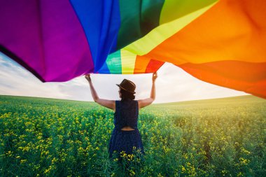 Yeşil bir çayırda elinde Gay Gökkuşağı Bayrağı tutan kadın. Aynı cinsiyet çiftleri için mutluluk, özgürlük ve aşk kavramı. 