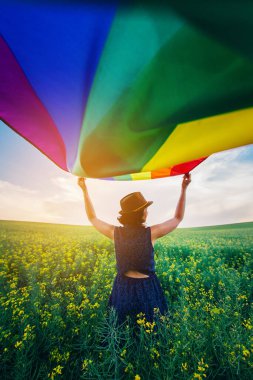 Yeşil bir çayırda elinde Gay Gökkuşağı Bayrağı tutan kadın. Aynı cinsiyet çiftleri için mutluluk, özgürlük ve aşk kavramı. 