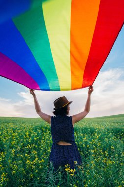 Yeşil bir çayırda elinde Gay Gökkuşağı Bayrağı tutan kadın. Aynı cinsiyet çiftleri için mutluluk, özgürlük ve aşk kavramı. 