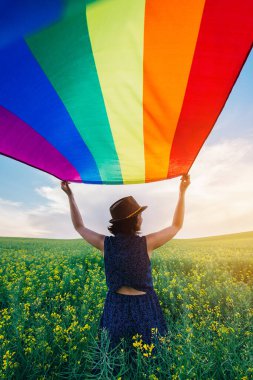 Yeşil bir çayırda elinde Gay Gökkuşağı Bayrağı tutan kadın. Aynı cinsiyet çiftleri için mutluluk, özgürlük ve aşk kavramı. 