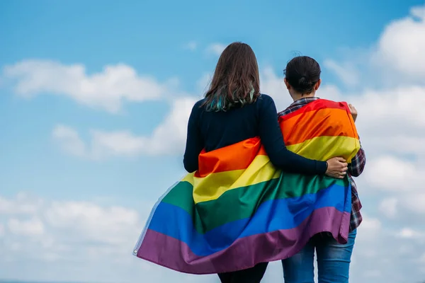 Lezbiyen çift dışarıda sarılıyor. LGBT gökkuşağı bayrağı.
