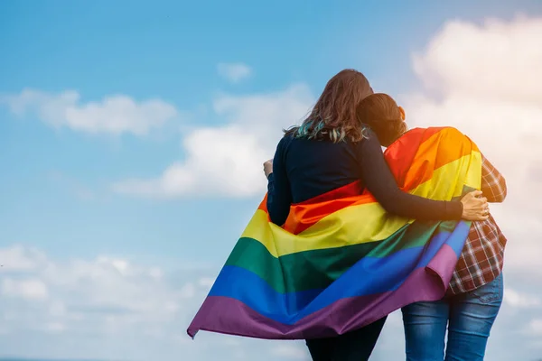 Lezbiyen çift dışarıda sarılıyor. LGBT gökkuşağı bayrağı.