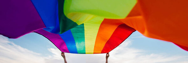 Woman holding the Gay Rainbow Flag on a green meadow outdoors. Happiness, freedom and love concept for same sex couples. 