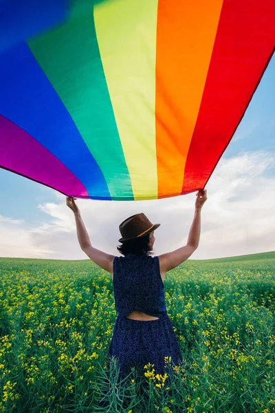 Yeşil bir çayırda elinde Gay Gökkuşağı Bayrağı tutan kadın. Aynı cinsiyet çiftleri için mutluluk, özgürlük ve aşk kavramı. 