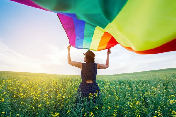 Woman holding the Gay Rainbow Flag on a green meadow outdoors. Happiness, freedom and love concept for same sex couples.