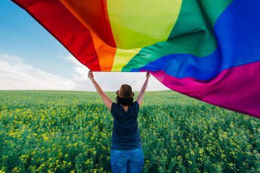 Yeşil bir çayırda elinde Gay Gökkuşağı Bayrağı tutan kadın. Aynı cinsiyet çiftleri için mutluluk, özgürlük ve aşk kavramı. 