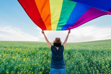 Yeşil bir çayırda elinde Gay Gökkuşağı Bayrağı tutan kadın. Aynı cinsiyet çiftleri için mutluluk, özgürlük ve aşk kavramı. 