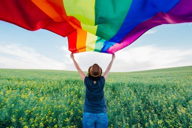 Yeşil bir çayırda elinde Gay Gökkuşağı Bayrağı tutan kadın. Aynı cinsiyet çiftleri için mutluluk, özgürlük ve aşk kavramı. 