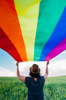Yeşil bir çayırda elinde Gay Gökkuşağı Bayrağı tutan kadın. Aynı cinsiyet çiftleri için mutluluk, özgürlük ve aşk kavramı. 