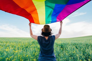 Yeşil bir çayırda elinde Gay Gökkuşağı Bayrağı tutan kadın. Aynı cinsiyet çiftleri için mutluluk, özgürlük ve aşk kavramı. 