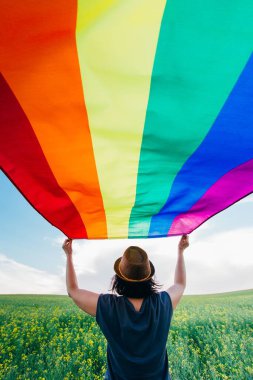 Yeşil bir çayırda elinde Gay Gökkuşağı Bayrağı tutan kadın. Aynı cinsiyet çiftleri için mutluluk, özgürlük ve aşk kavramı. 