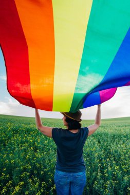 Yeşil bir çayırda elinde Gay Gökkuşağı Bayrağı tutan kadın. Aynı cinsiyet çiftleri için mutluluk, özgürlük ve aşk kavramı. 