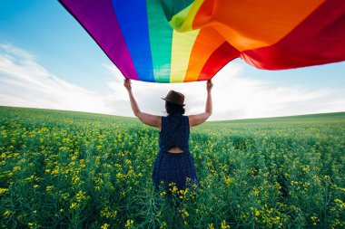 Yeşil bir çayırda elinde Gay Gökkuşağı Bayrağı tutan kadın. Aynı cinsiyet çiftleri için mutluluk, özgürlük ve aşk kavramı. 