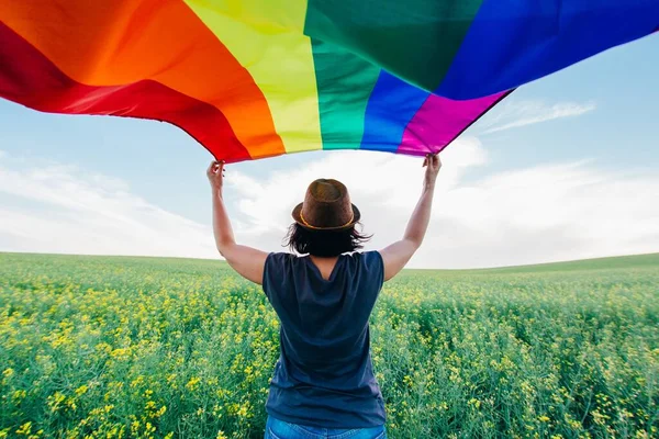女性は屋外の緑の牧草地にゲイレインボーフラッグを保持 同じセックスカップルのための幸福 自由と愛の概念 — ストック写真