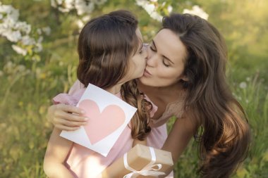 Anneler günün kutlu olsun! kızı tekrar anne öpüşme ve kart ve hediye verir. Doğum günün kutlu olsun. İnsanlar, tatiller ve aile konsepti-mutlu kızı ve anne çiçek lenme arka plan karşı