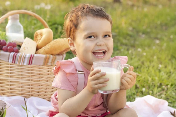 Happy child drinks milk. A picnic in the blooming flowers. Happy birthday! people, holidays and family concept - happy kids