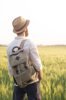 Gün batımında buğday tarlasında sırt çantası olan gezgin. Açık ufkun arka planında doğada insan. Özgürlük ve keşif kavramı. Çevre ve yaşam tarzı