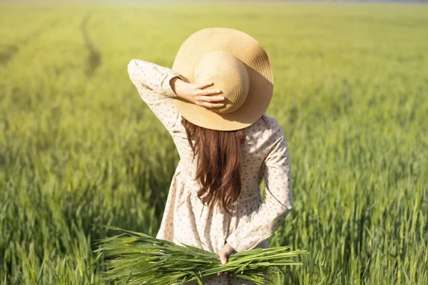 A beautiful woman in a straw hat stands against the sun in a field of wheat. Farmer on the background of nature with ears of raw wheat in his hands . The concept of beauty and care for yourself and the world. Environment and way of life. Organic farm