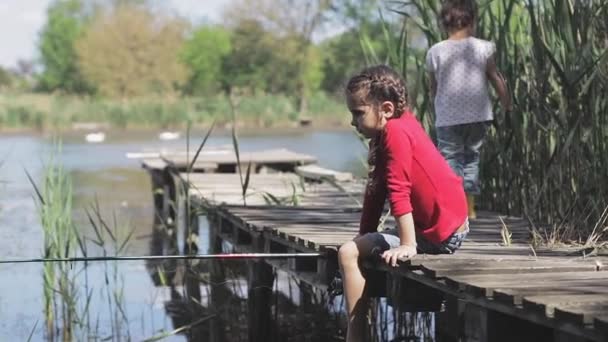 Child fishing girl on the lake at the pier. Throws and pulls the fishing rod spinning. — Stock Video