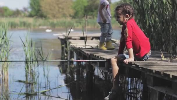 Enfant fille de pêche sur le lac à la jetée. Jette et tire la canne à pêche filature . — Video