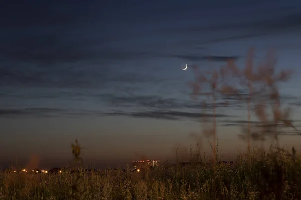 Night sky in the city. Young moon in the evening dark sky