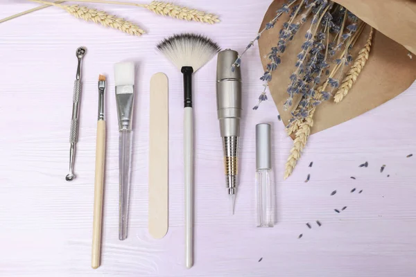 Cosmetology tools: aesthetics, eyebrow tattoo brush, scissors, cream tube, jar on a light background