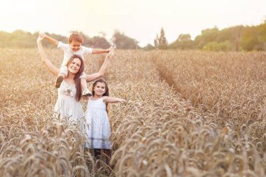 Mutlu aile, anne, oğul ve gün batımında buğday tarlasında hasır şapkalı kız. Organik tarım ve sağlıklı yaşam tarzı, sağlıklı gıda, mutluluk ve sevinç kavramı