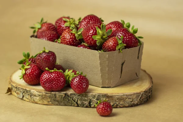 Fresh strawberries in a Kraft box on a wooden stand close-up. Open space, healthy food concept, plants, soil, organic natural products, natural food, vegetarian dishes, vegetables, raw, food festival
