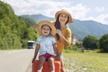 Yaz aylarında mutlu aile dinlenmek için gider, tatilde: anne ve oğlu doğanın ve dağların arka planda bir bavul ile