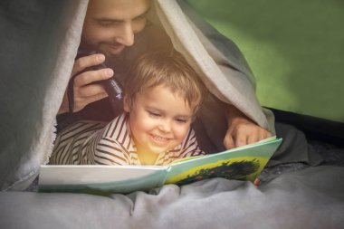 Babalar günü. Neşeli baba ve oğul doğada birlikte tatilde, kampta, çadırda seyahat ediyor. mutlu aile baba ve çocuk oğlu doğada bir çadırda bir el feneri ile bir kitap okuma