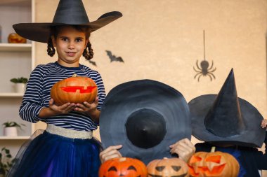 Mutlu aile: baba, kardeş Cadılar Bayramı 'nı kutluyor. Karnaval kostümlü neşeli çocuklar içeride. Neşeli çocuklar ve ebeveynler balkabakları ve siyah cadı şapkalarıyla oynuyorlar.